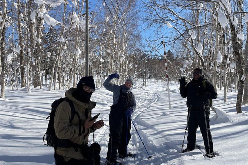 Three people skiing in a snowy forest with bare trees and a clear sky. 3
