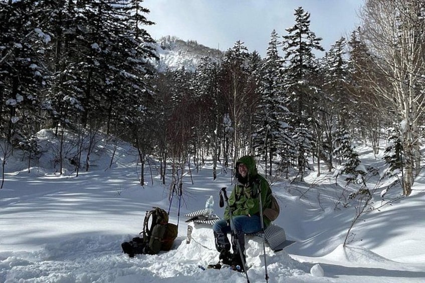 A person sitting on the snow in a forest with trees and a mountain in the background. 4