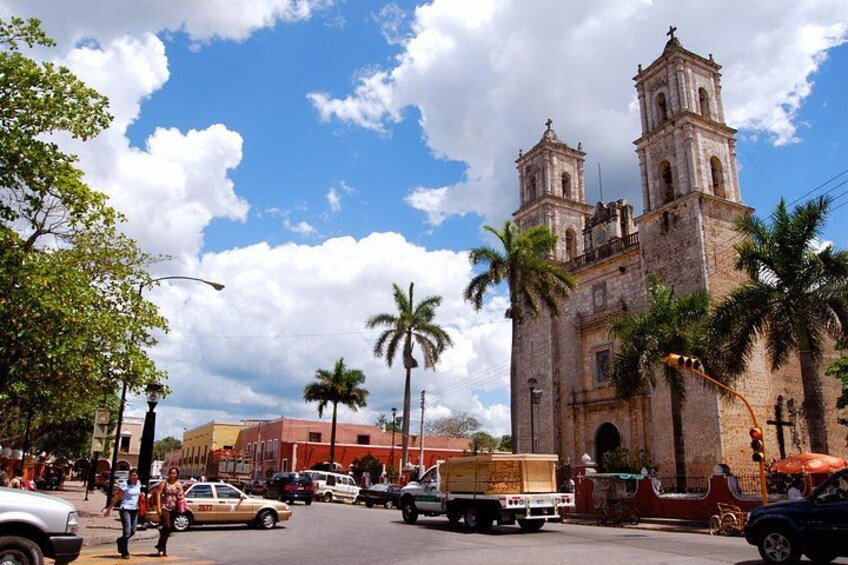 Una iglesia histórica con dos torres de campanas, palmeras y una calle concurrida con coches y peatones. 4
