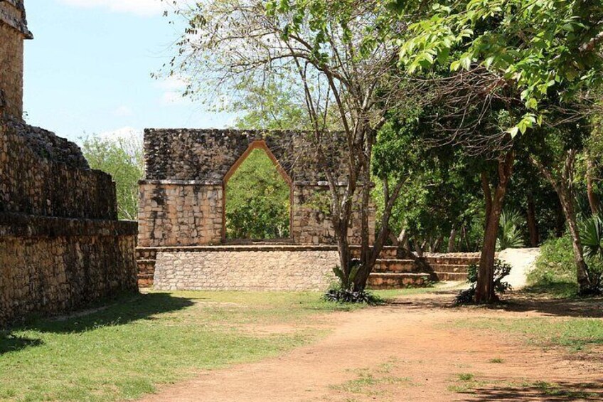 An ancient stone structure with a pointed arch, surrounded by trees and a dirt path. 3