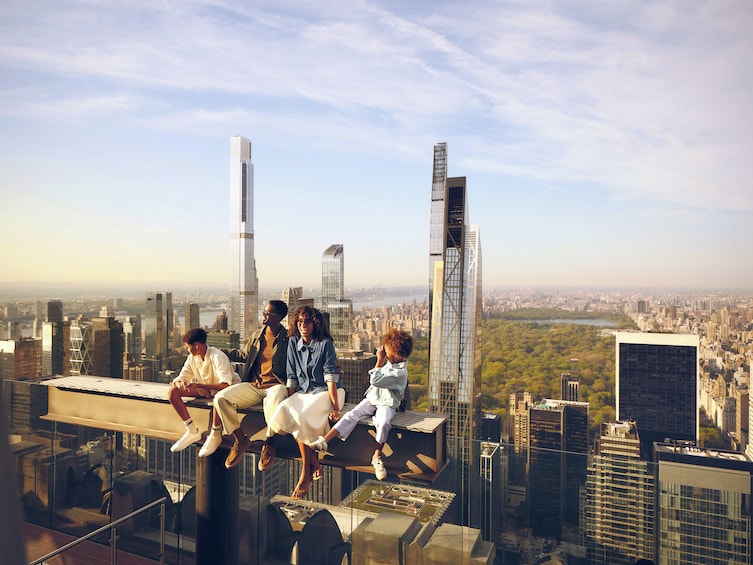 A group of people sitting on a rooftop with a cityscape in the background. 1