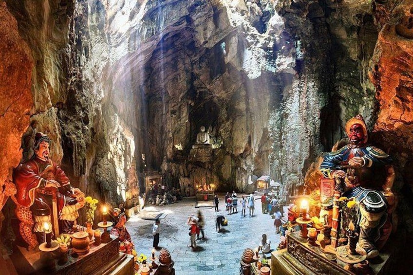 A cave with statues, a large Buddha, and people. 3