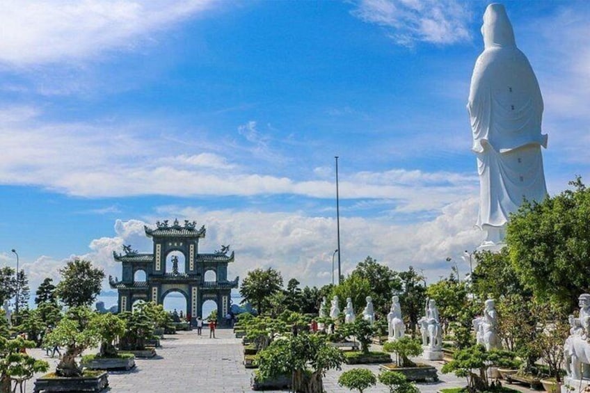 A traditional gate, a large white statue, and numerous smaller statues in a landscaped garden. 3