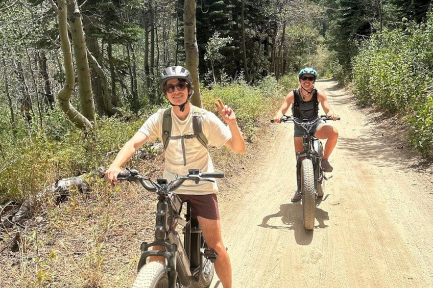 Two cyclists on a dirt path surrounded by trees. 4