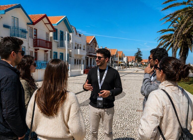 A group of people standing on a cobblestone street with buildings featuring red-tiled roofs and balconies. 4