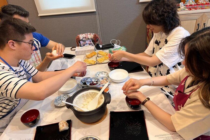 Menschen sitzen an einem Tisch mit Schüsseln, Essstäbchen und einem Topf voller Essen. 1