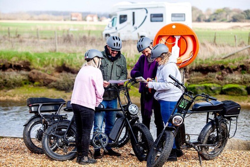 A group of people around bicycles near a river with a trailer in the background. 3