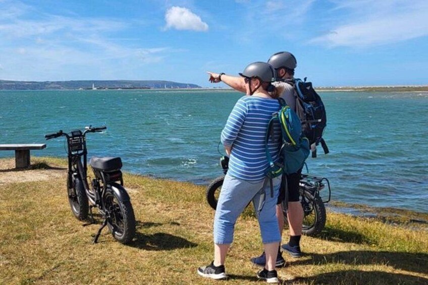 A lake with a bench, a motorcycle, and two people with helmets and backpacks. 1