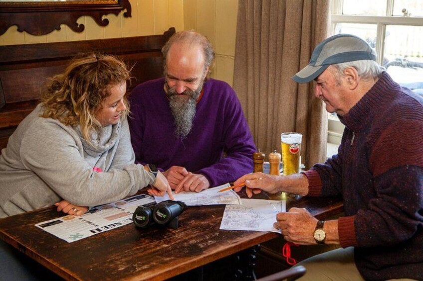 Three people sitting at a wooden table with papers, a beer mug, and a bottle. 2