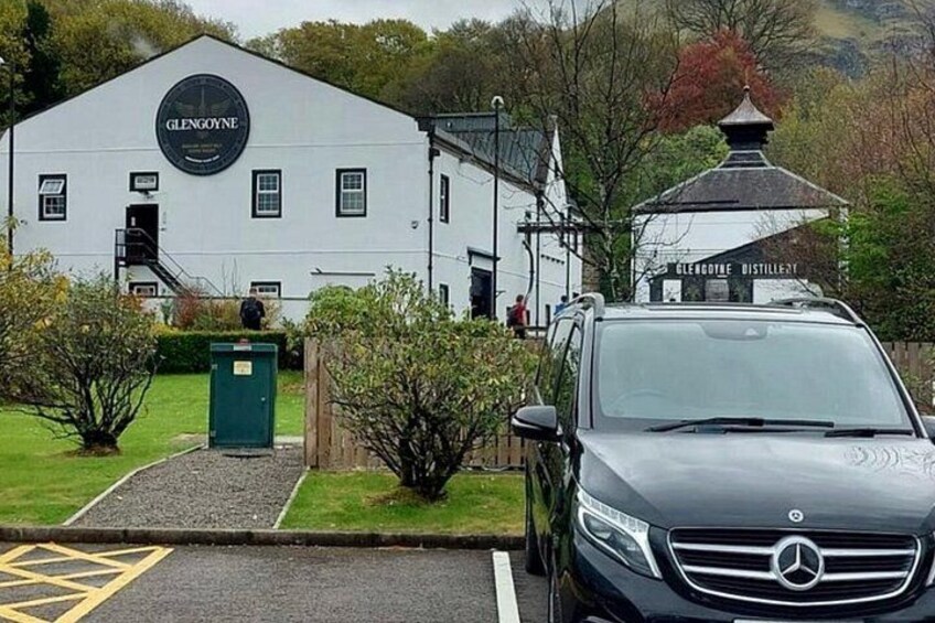 Un edificio blanco con un letrero que dice 'GLENGOYNE DISTILLERY' y un coche estacionado adelante. 2