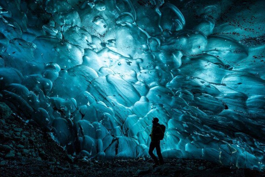 Une personne se tient devant une vaste grotte de glace, ornée de formations complexes. 3
