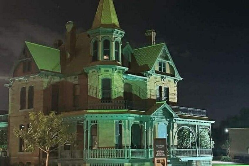 A large, historic building with a prominent tower and green-lit facade at night. 1