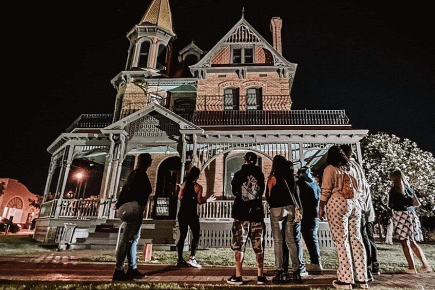 A historic building with a prominent tower and a porch with people standing around it. 2