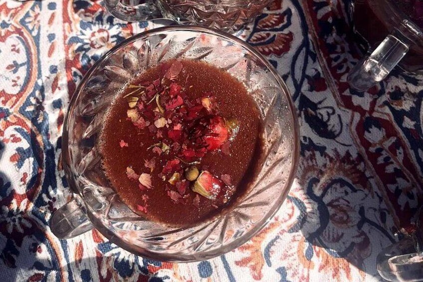 Una ciotola di vetro con un liquido scuro, guarnita con condimenti rossi e verdi, su un tessuto decorato. 3