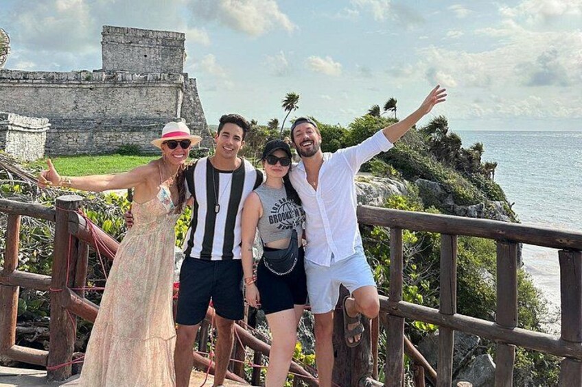 A group of people on a wooden bridge with a historical stone structure in the background. 1