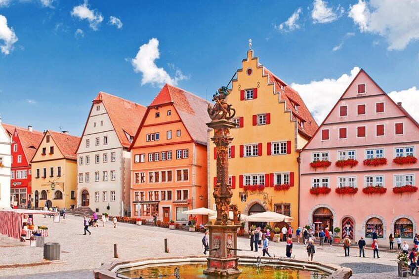 A town square with colorful buildings, a fountain, and people walking. 4