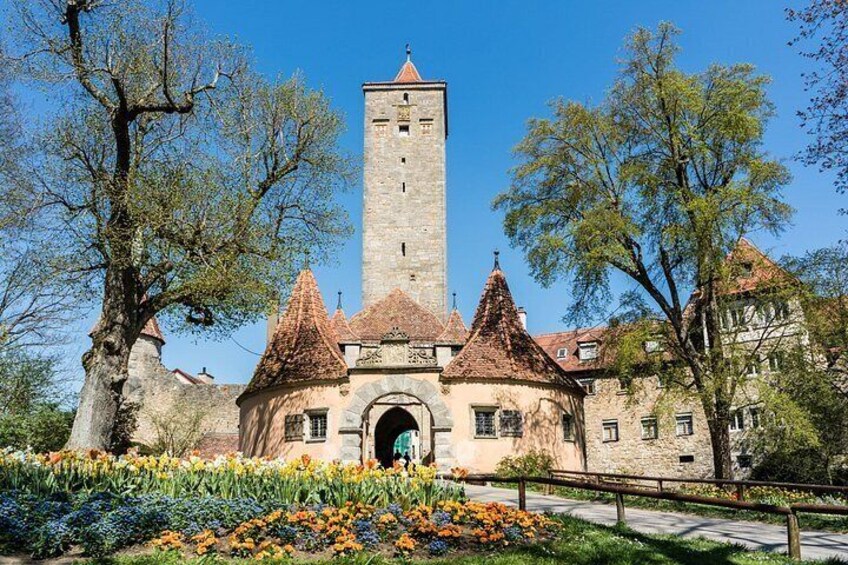A historic building with a tall tower, surrounded by trees and a flower garden. 4