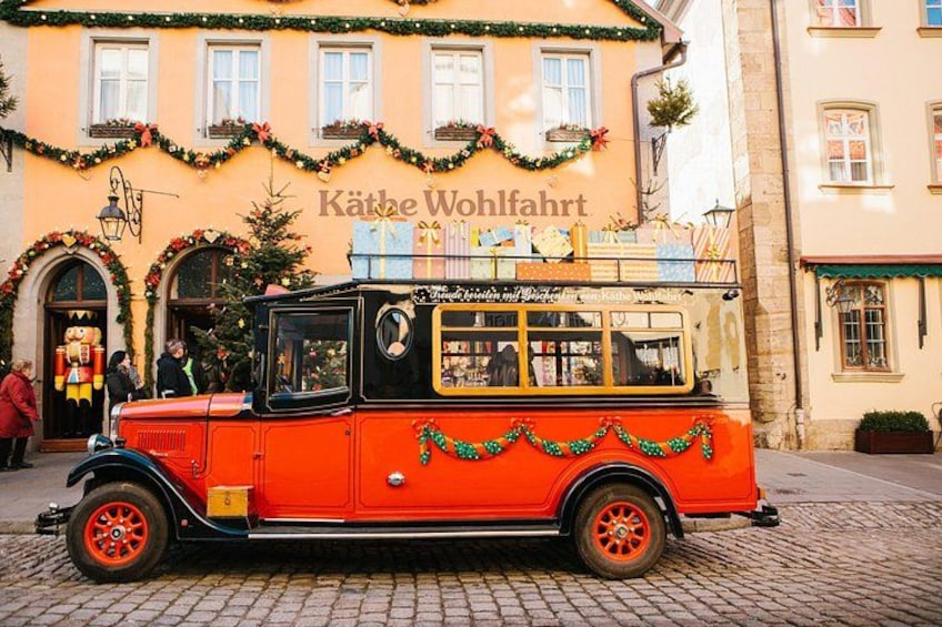 A vintage red car with a black roof parked in front of a building with Christmas decorations. 2