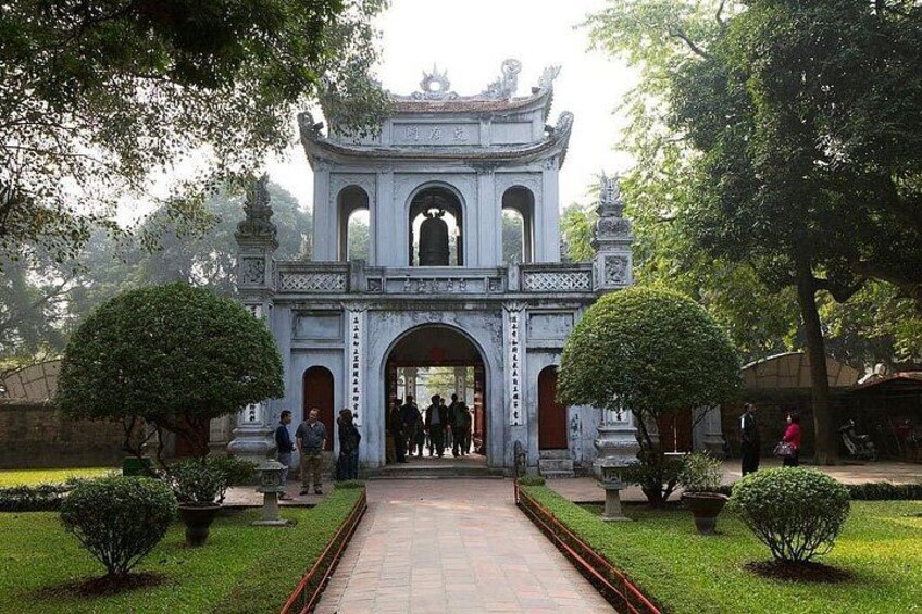 A traditional gate with intricate carvings, surrounded by well-maintained greenery and a paved pathway leading through it. 3