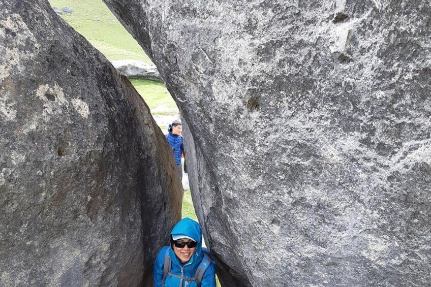 A person in a blue jacket and hat walking through a narrow rock passage. 5
