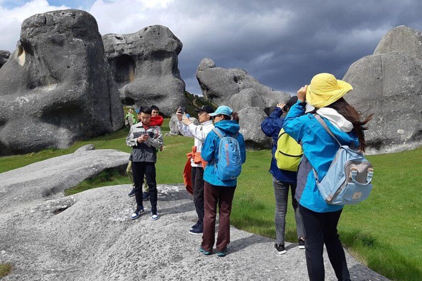 People standing on a rocky path with large boulders and a grassy area in the background. 4