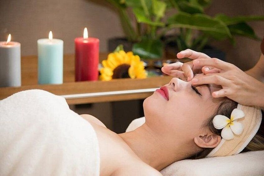 A person receiving a facial treatment with candles and flowers in the background. 3
