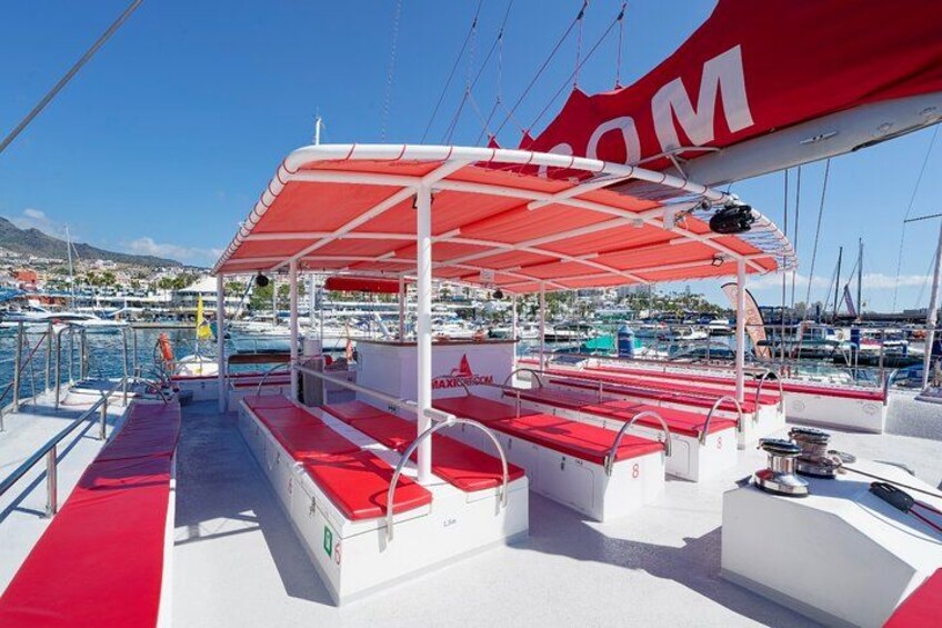 A boat deck with red and white seating, a canopy, and a marina in the background. 5