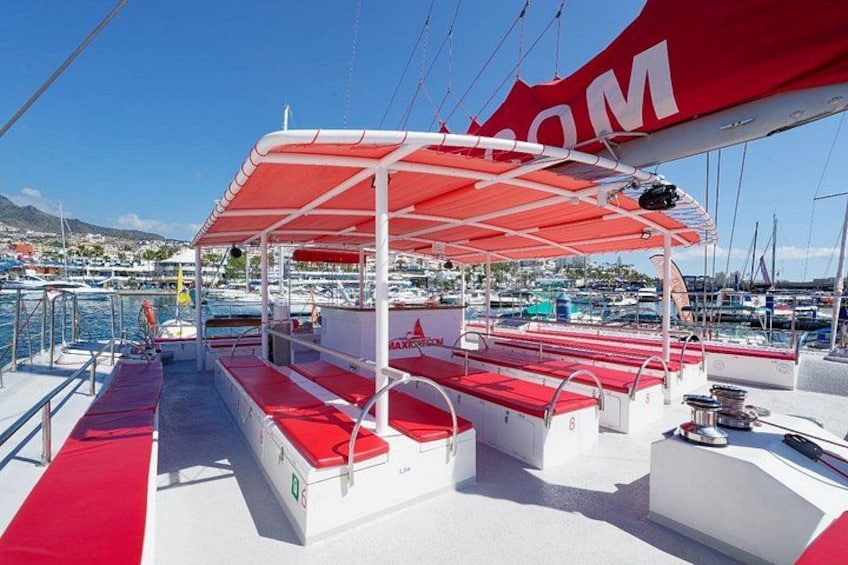 A boat deck with red and white seating, a canopy, and a marina in the background. 5