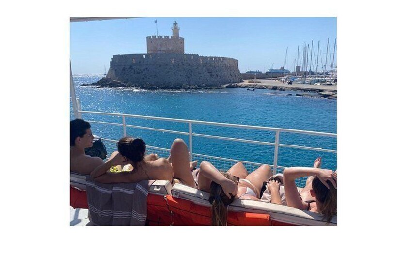 People relaxing on a boat with a historic fort and sailboats in the background. 2