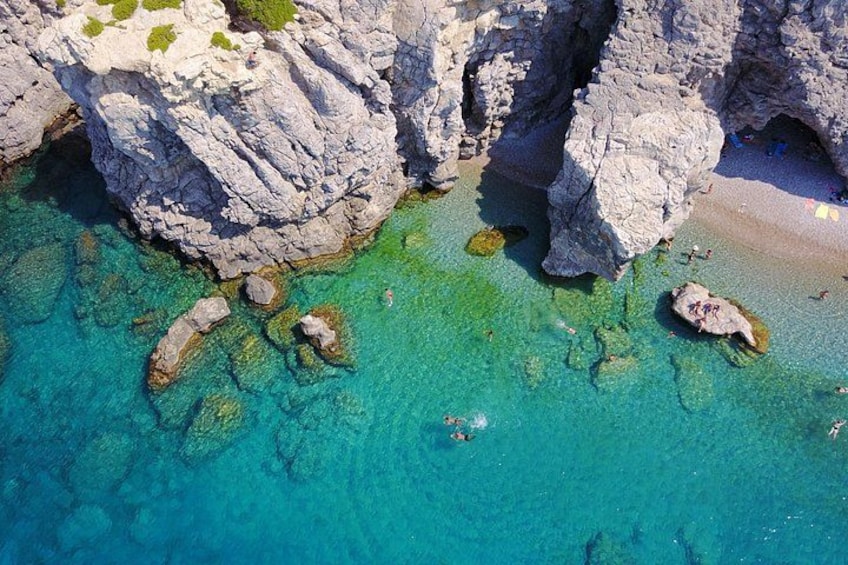 A coastal landscape with rocky cliffs, clear turquoise waters, and a sandy beach. 4