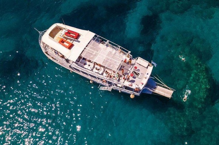 An aerial view of a boat with a deck, passengers, and clear blue water. 1