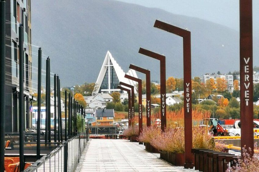 A pathway lined with tall metal structures and a modern building in the background. 1