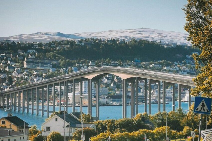 A bridge over a body of water with a town in the background and snow-capped mountains. 4