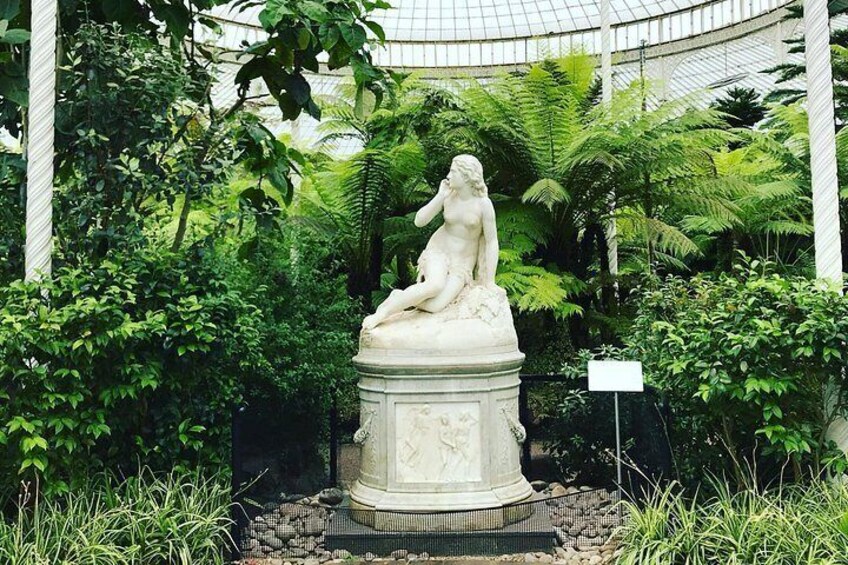 A classical statue in a garden with lush greenery and a glass-domed structure in the background. 5