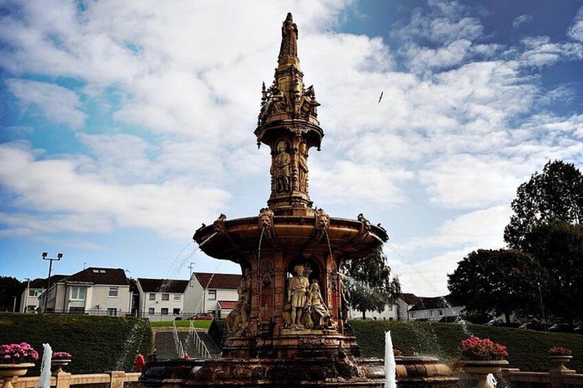 A large ornate fountain with statues, surrounded by a landscaped garden and residential buildings in the background. 5