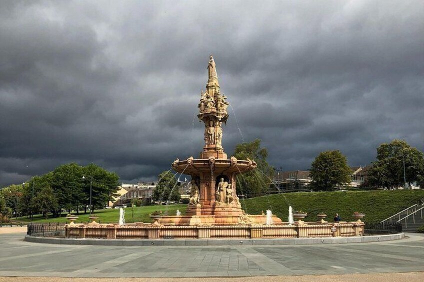 A large, ornate fountain with statues in the center, surrounded by a circular plaza and a fence. 3