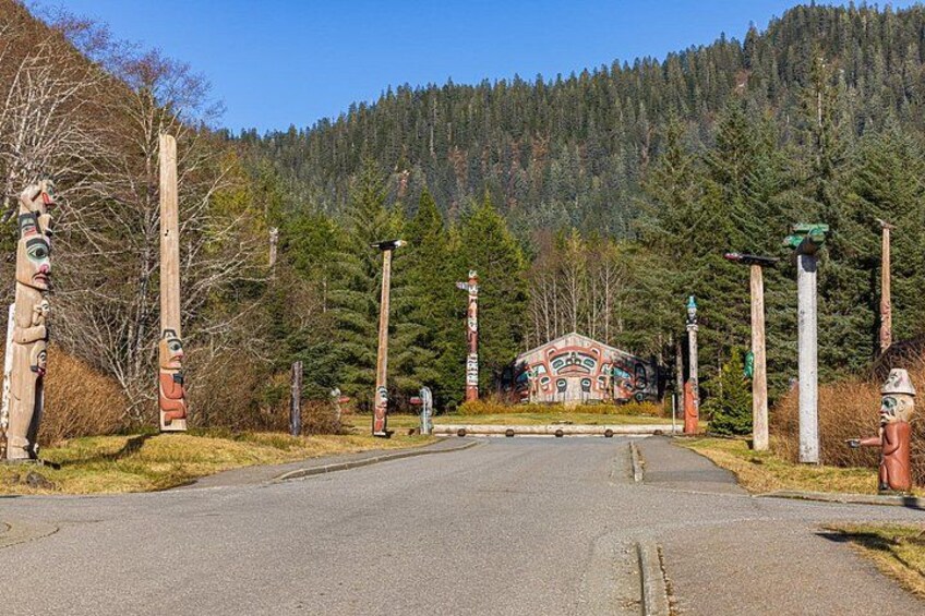 Une route menant à un bâtiment à la façade colorée, entouré de totems et d’une forêt dense. 2