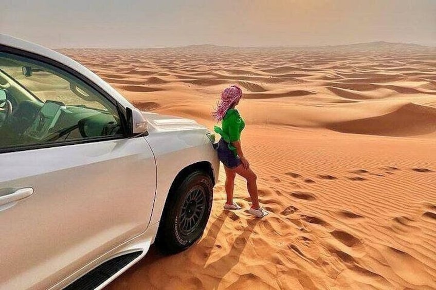 A white car parked on a sandy desert with a person standing beside it. 2