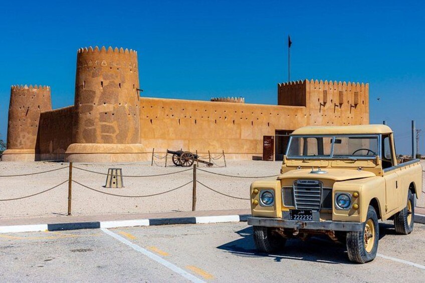 A yellow off-road vehicle parked in front of a historical fort with two large towers. 1