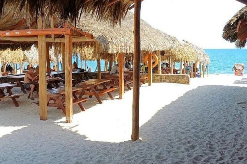 A beach with wooden picnic tables and thatched-roof structures. 1