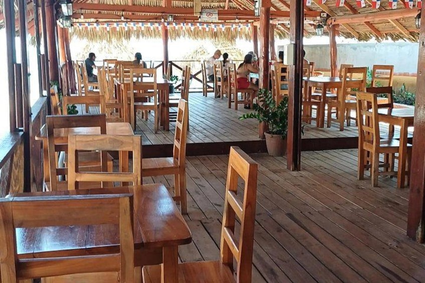 A wooden deck with tables and chairs, a thatched roof, and potted plants. 3