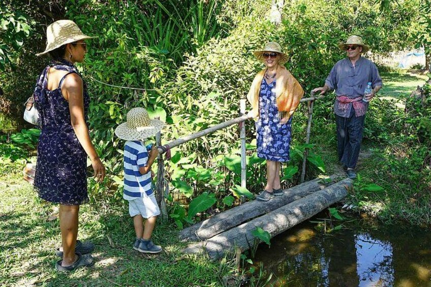 Un grupo de personas cruzando un puente de troncos sobre un pequeño cuerpo de agua en un entorno verde y frondoso. 2