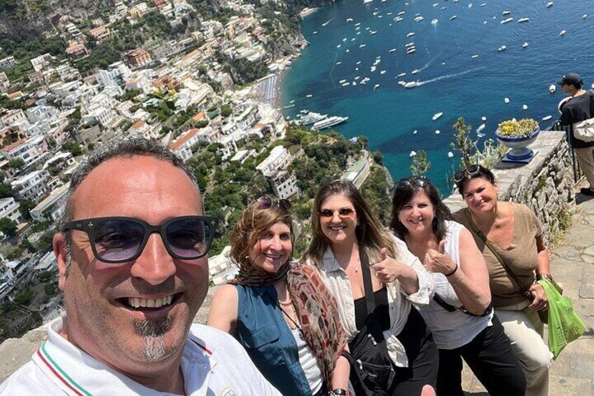 Un groupe de personnes se tient sur une falaise surplombant une ville côtière, avec des bateaux sur l’eau. 5
