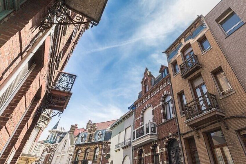 A street with historic buildings, including a building with a balcony and a sign with a pattern. 4