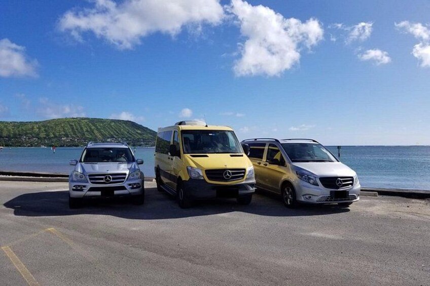 Three parked cars by a waterfront with a clear sky and a hilly landscape in the background. 4