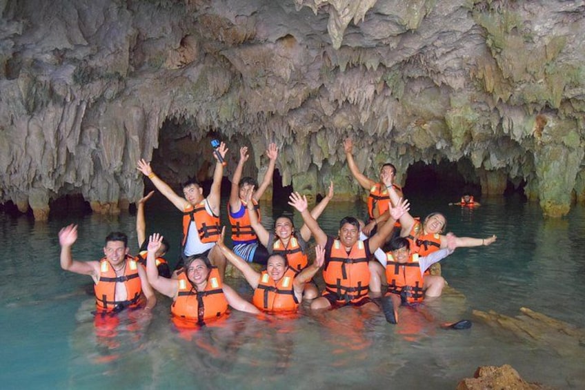 A group of people in orange life jackets in a cave with water. 2