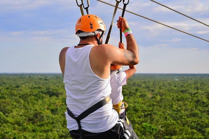 A person in a white tank top and orange helmet, harnessed and holding onto a zip line. 2