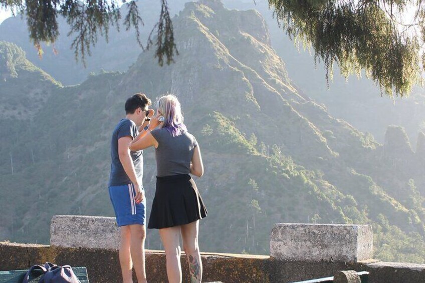 Two people standing on a ledge with a mountainous landscape in the background. 2