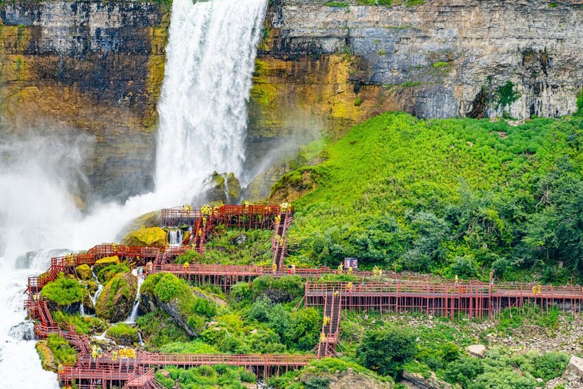 A waterfall cascading down a rocky cliff, surrounded by lush greenery and a red pedestrian bridge. 5
