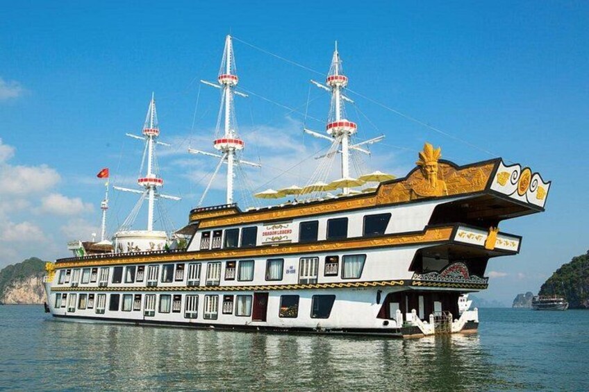 A large, multi-decked riverboat with multiple masts and flags, sailing on a body of water with a mountainous coastline in the background. 2